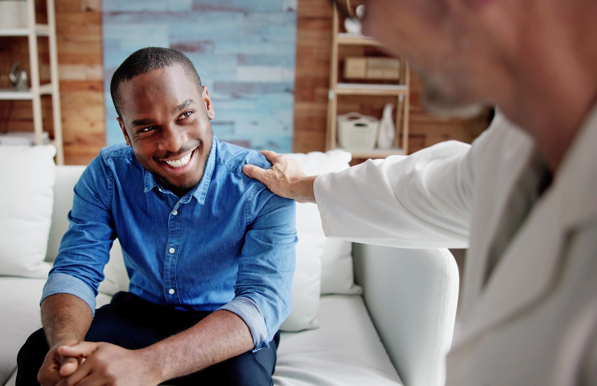 Healthcare provider in white coat placing reassuring hand on smiling man's shoulder during consultation