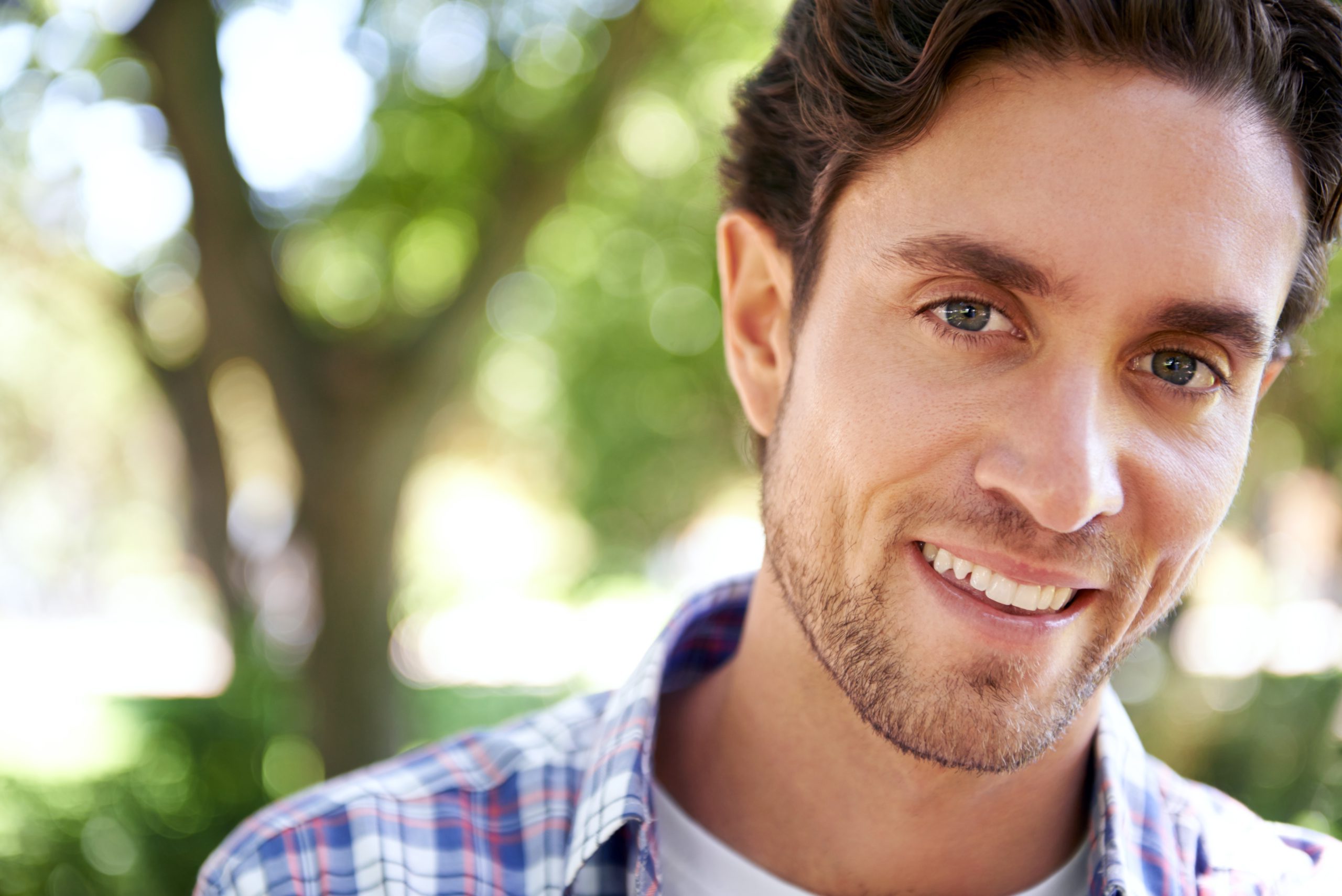 Man smiling outdoors with blurred green foliage background