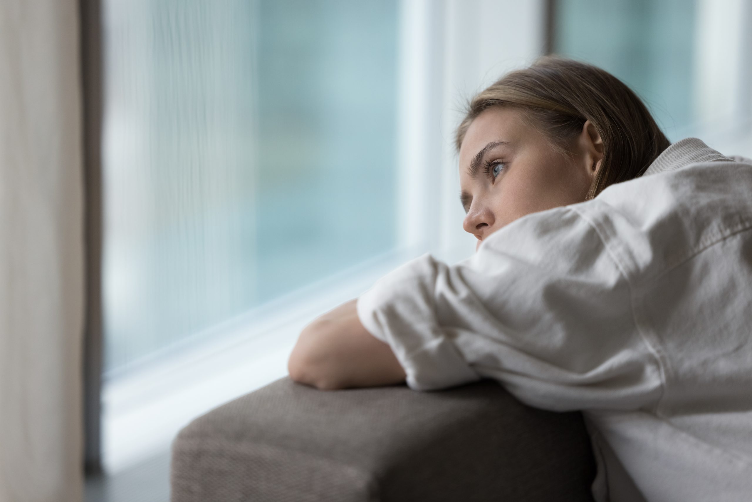 Woman leaning on window sill gazing outside, appearing contemplative or worried