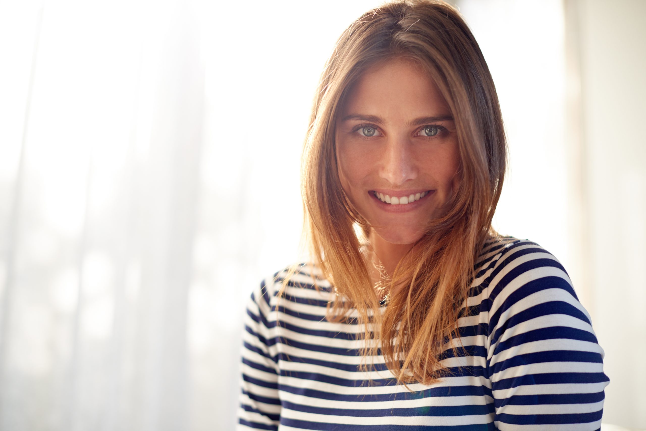Woman with reddish-brown hair wearing navy and white striped shirt, smiling in bright room