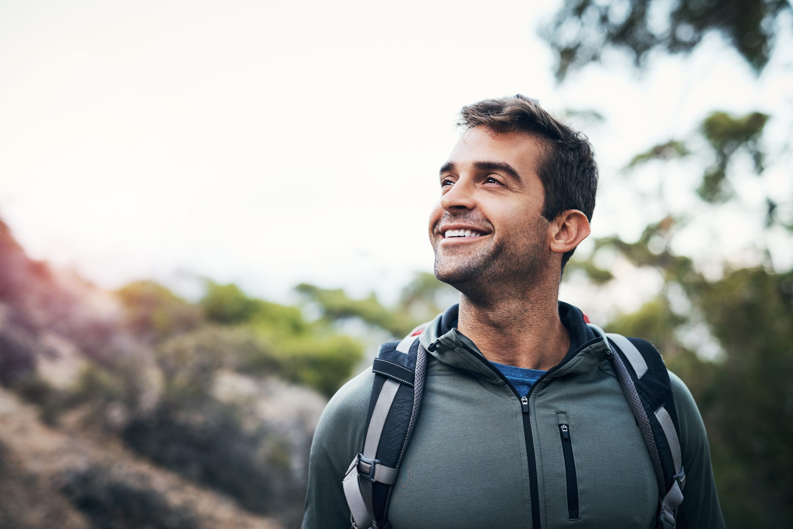Man in hiking gear smiling outdoors with trees and sky in background