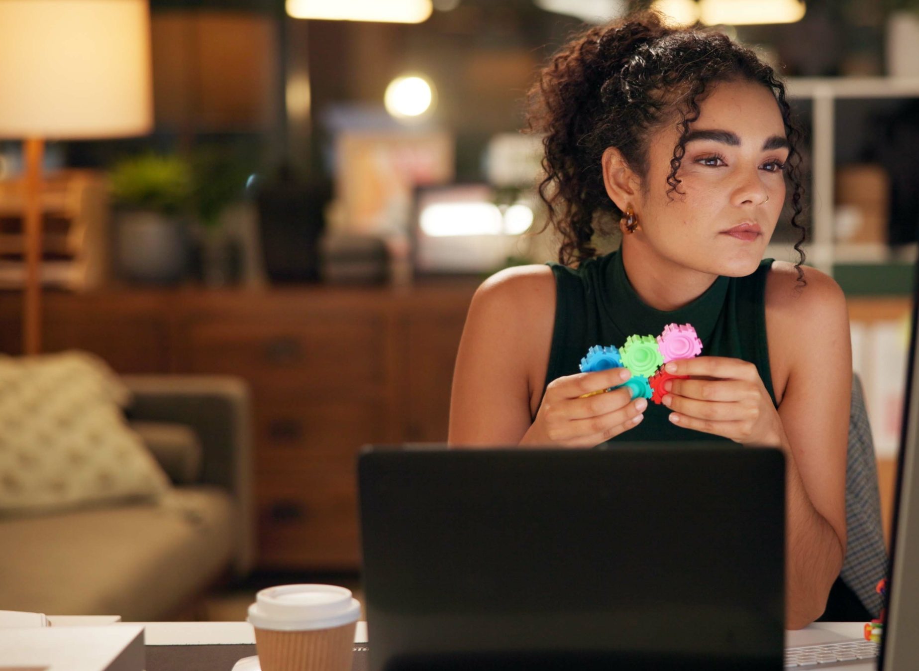 Woman at laptop holding colorful stress relief fidget toys, appearing distressed while working