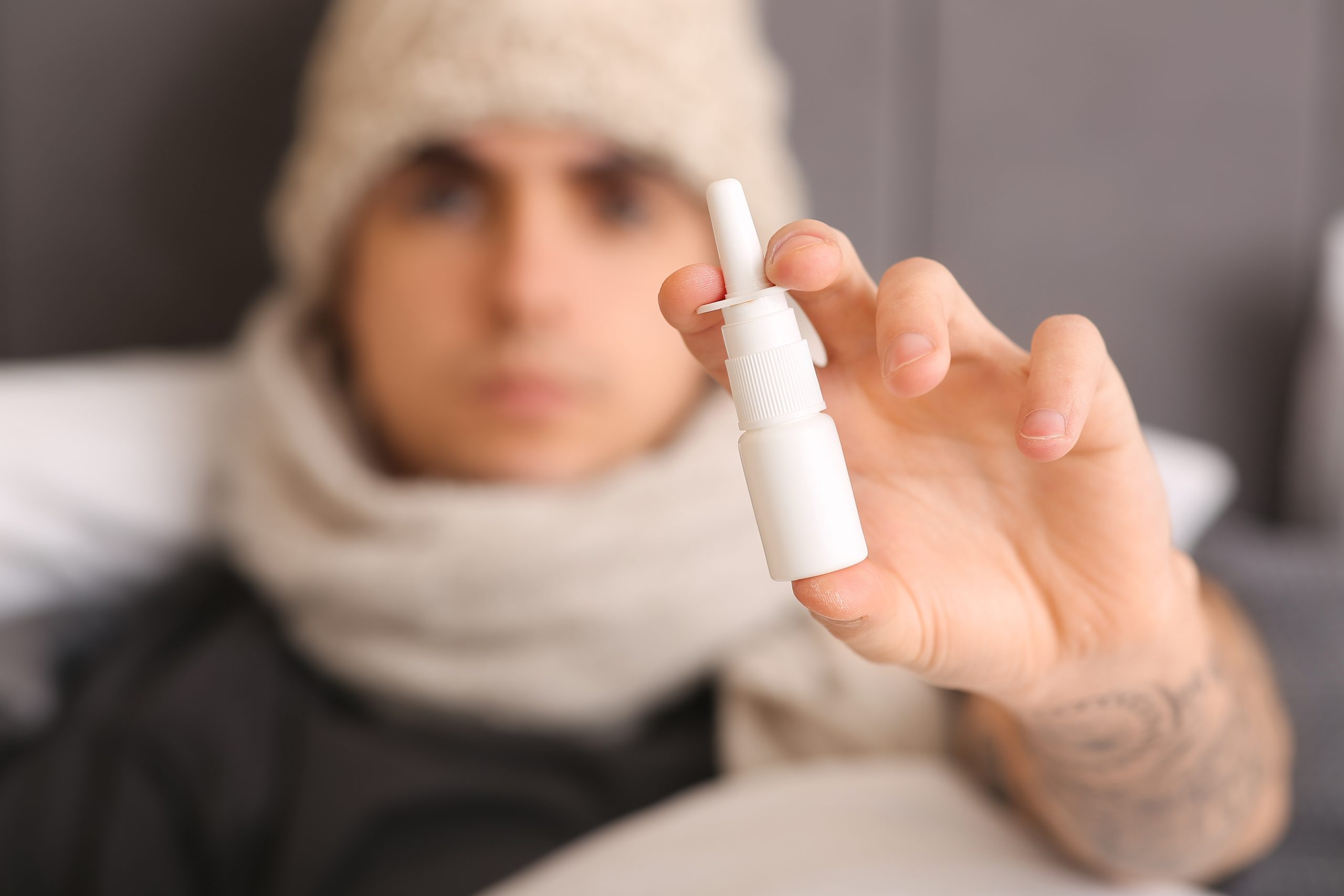 Person wearing white beanie and scarf holding up nasal spray bottle