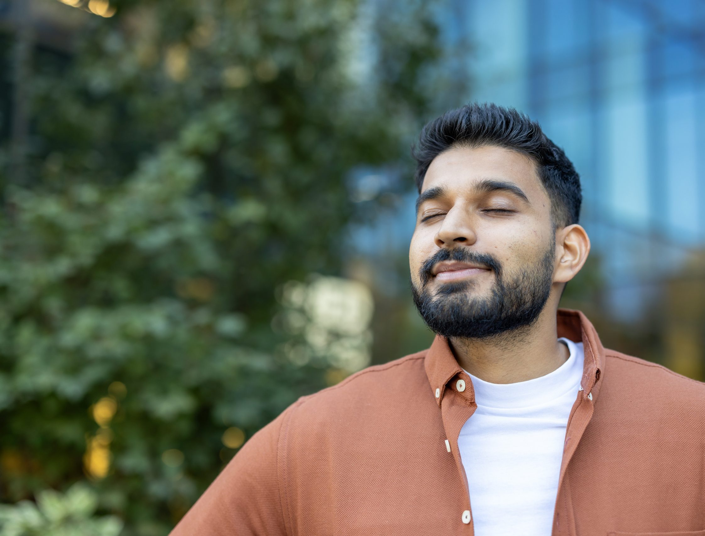 Man with eyes closed standing outdoors near greenery