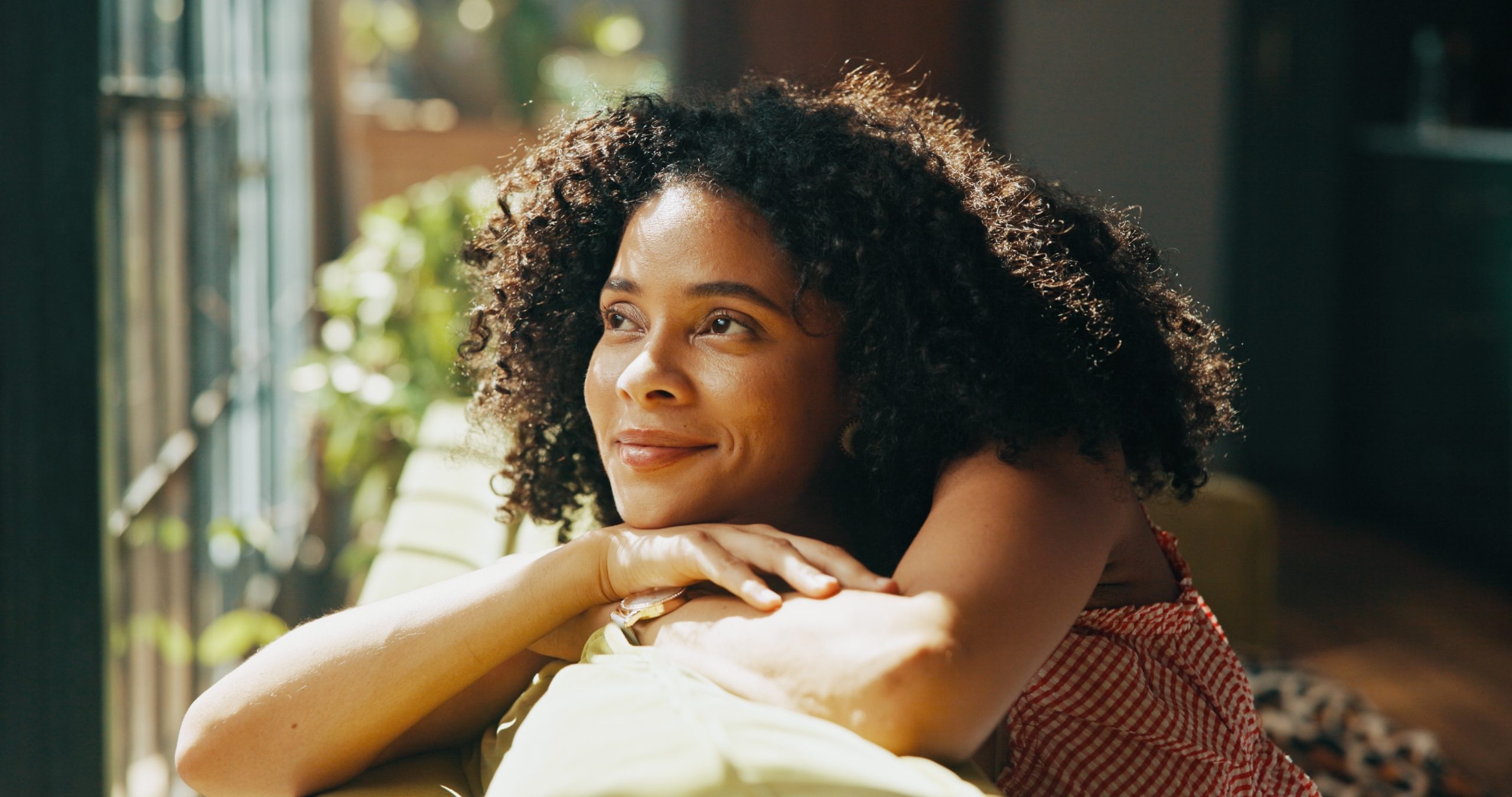 Woman with curly hair leaning on railing by window with natural light