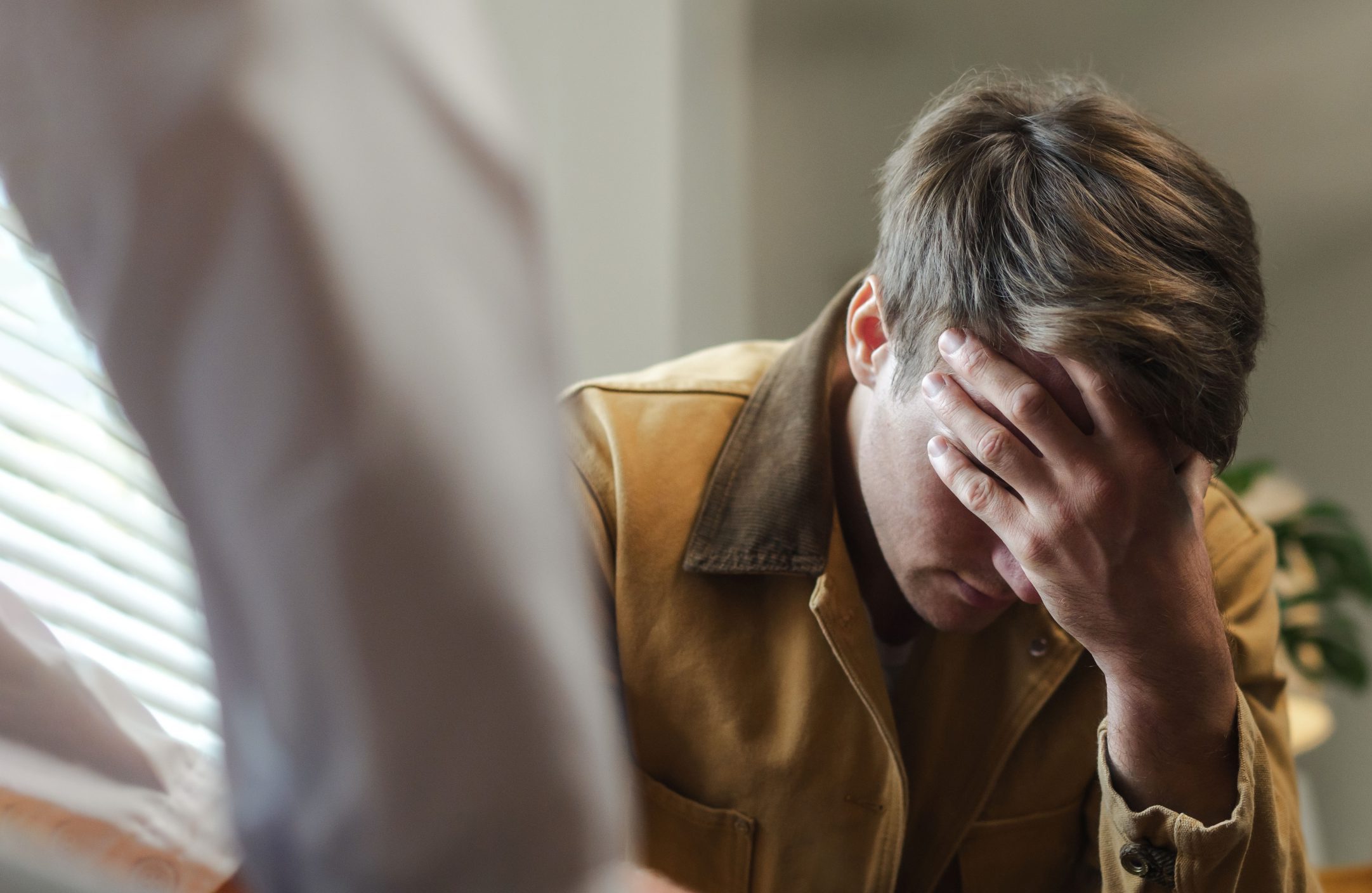 Man in brown shirt holding his head in distress during a consultation