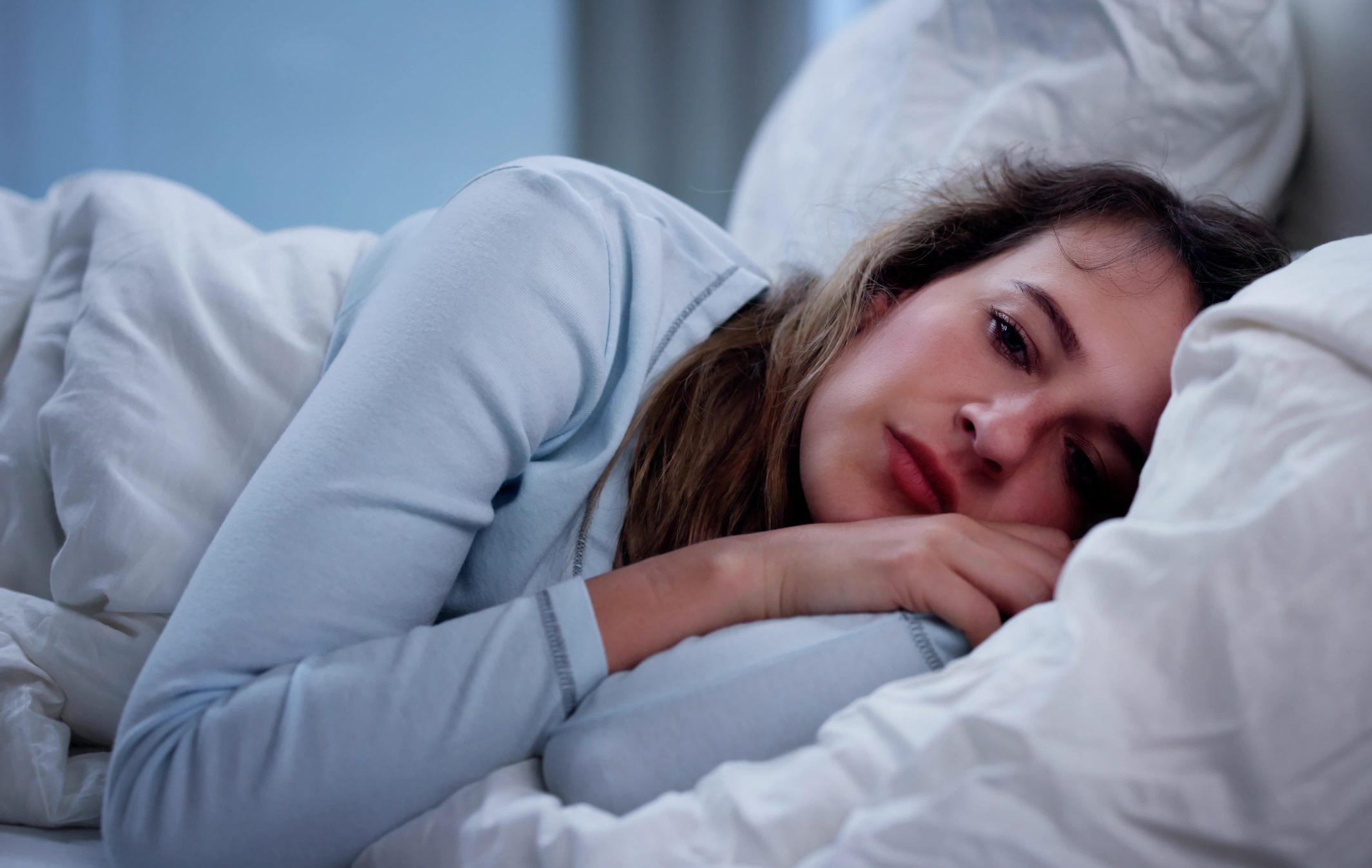 Woman in bed looking unwell while resting on pillows