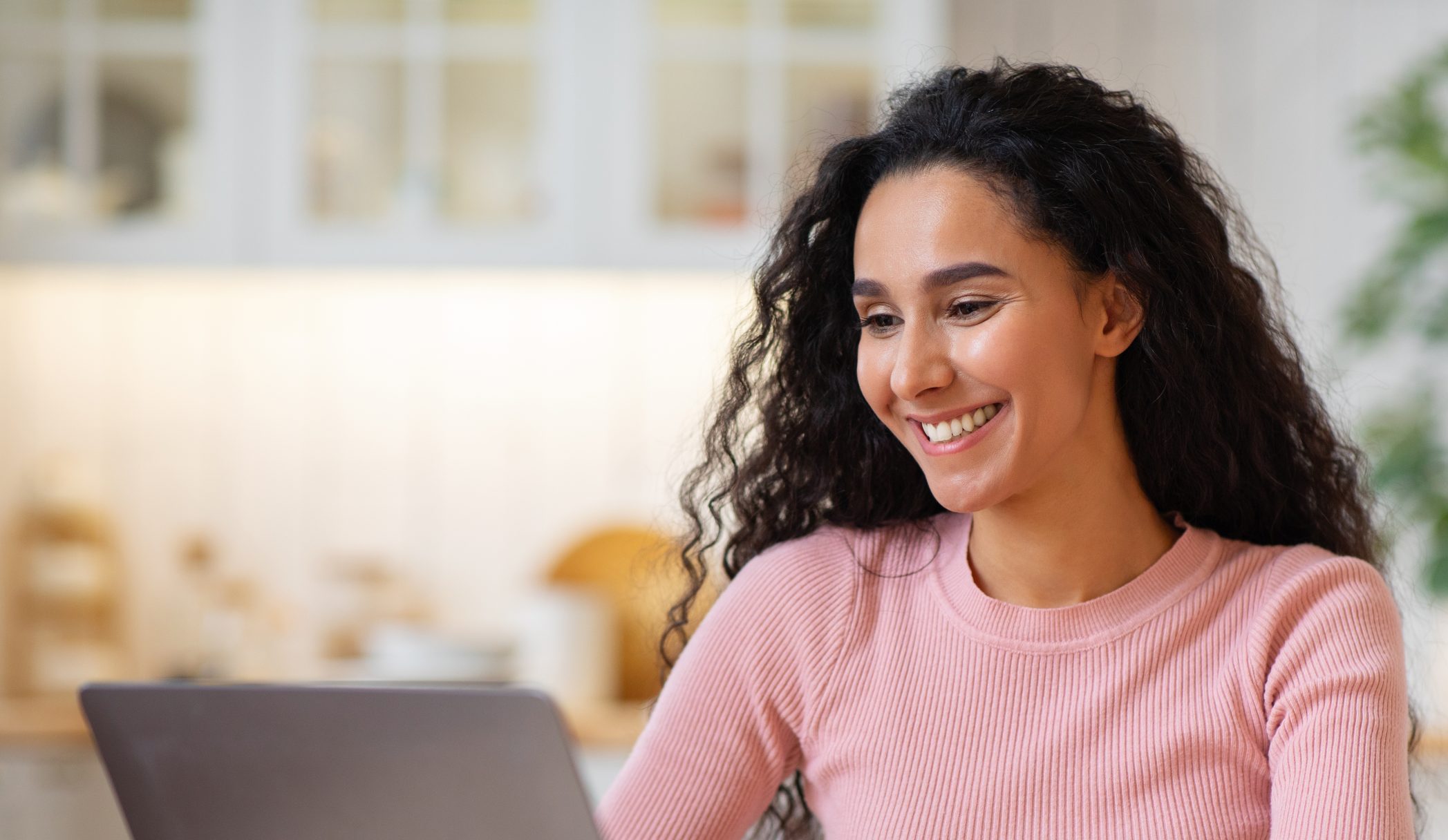Smiling woman with curly hair using laptop at home