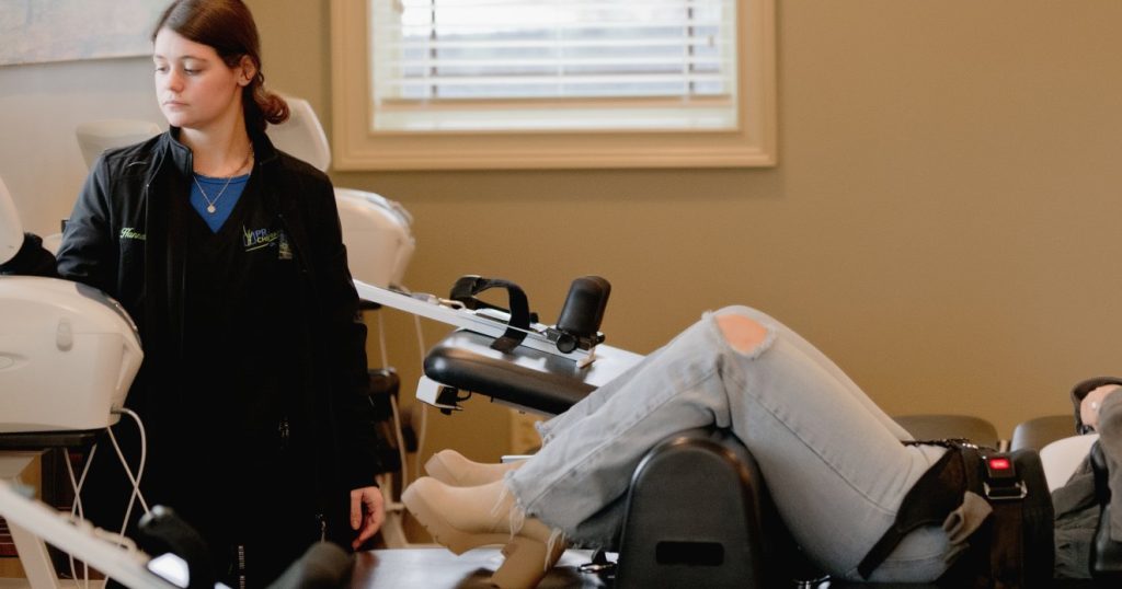Chiropractor in black jacket observing patient receiving spinal treatment on clinical table
