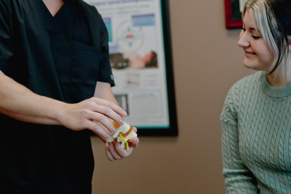 Chiropractor showing patient a spinal model during consultation in clinical office