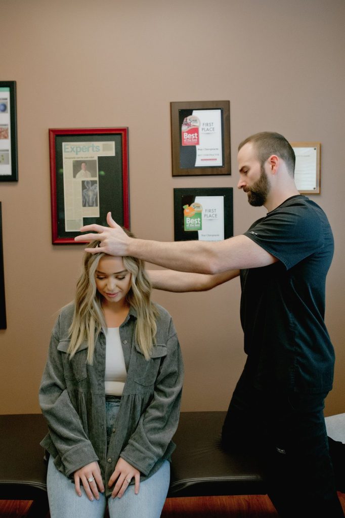 Chiropractor palpating patient's head and neck while patient sits in treatment room