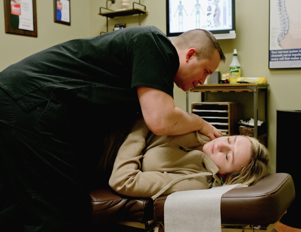 Chiropractor performing cervical spine adjustment on patient lying on treatment table