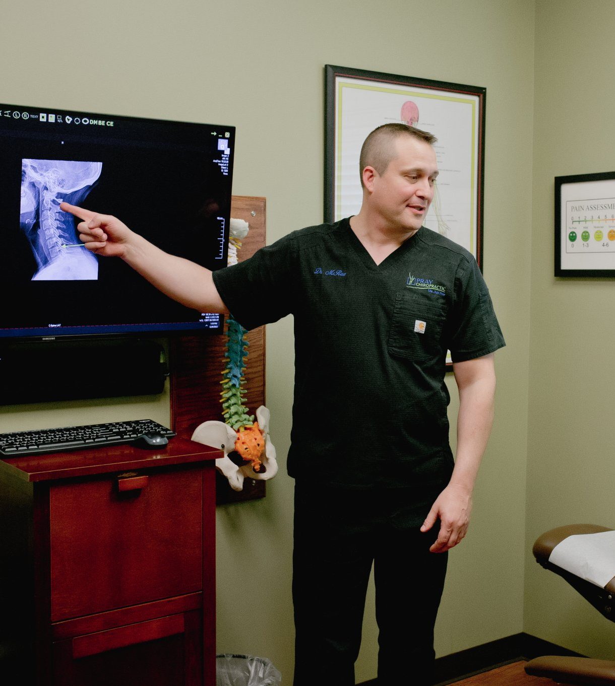 Chiropractor pointing to cervical spine X-ray on monitor during patient consultation