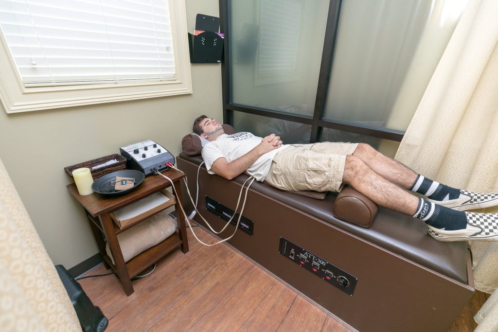 Patient lying on treatment table receiving electrical stimulation therapy with device on nearby table