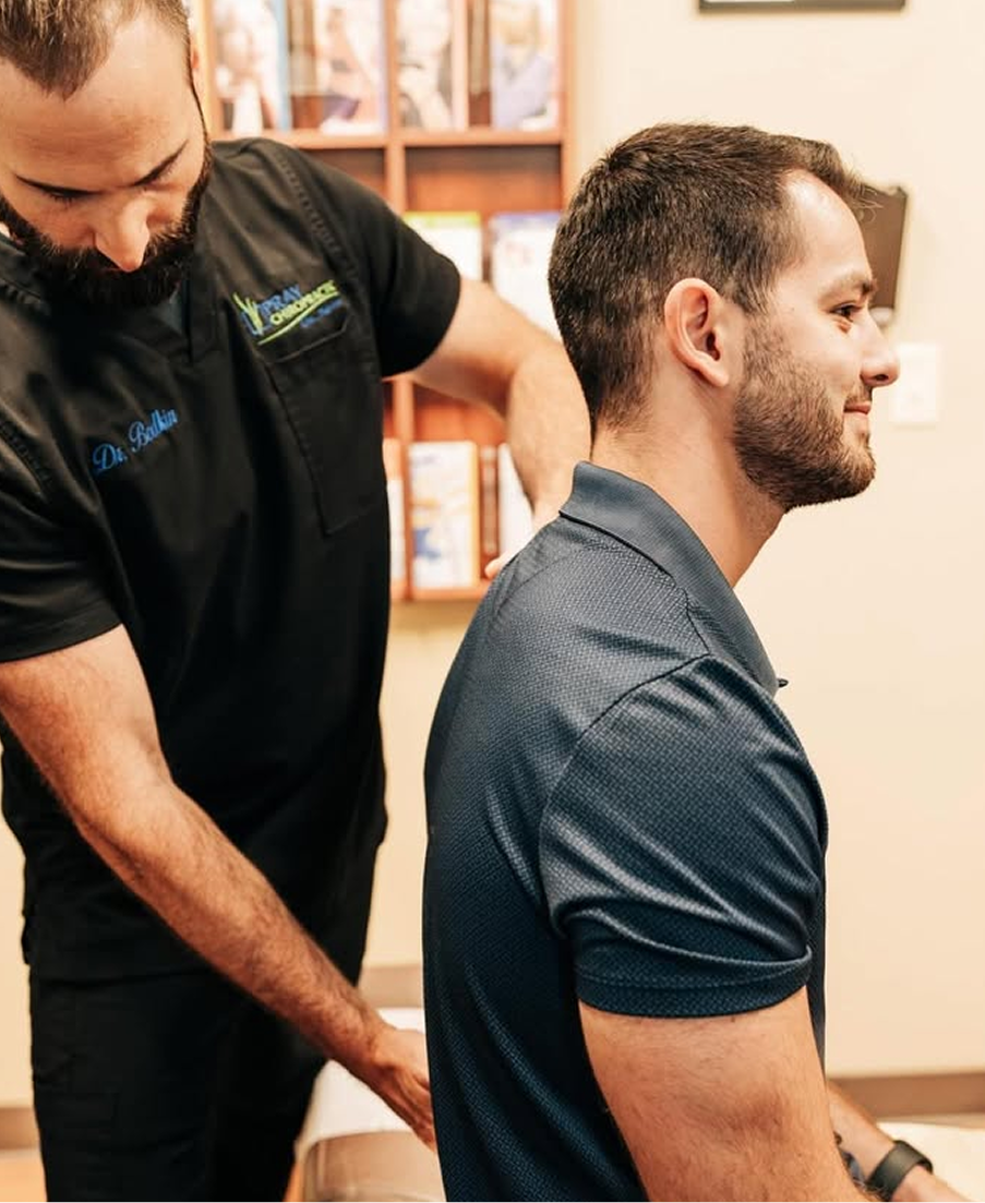 Chiropractor performing spinal adjustment on seated male patient in treatment room