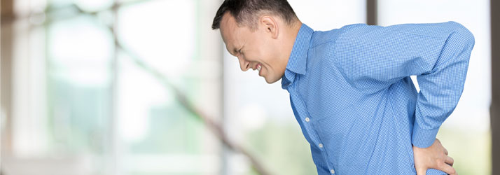Man in blue shirt bent forward holding lower back in pain