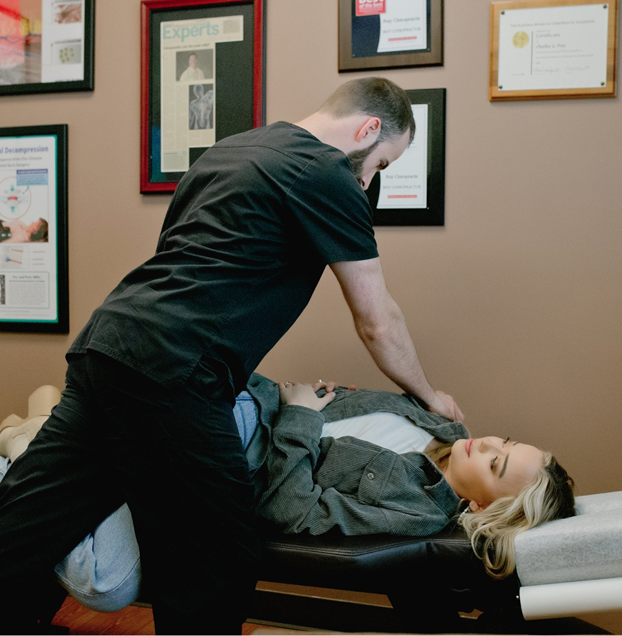 Chiropractor performing spinal adjustment on patient lying on treatment table