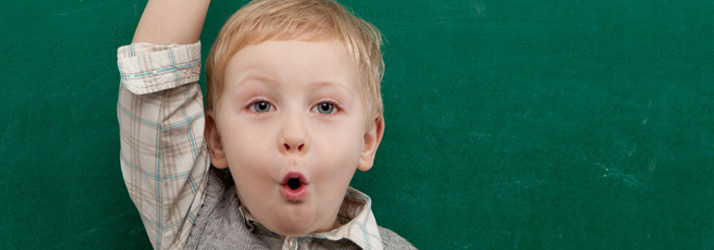 Young boy with arm raised against green chalkboard background