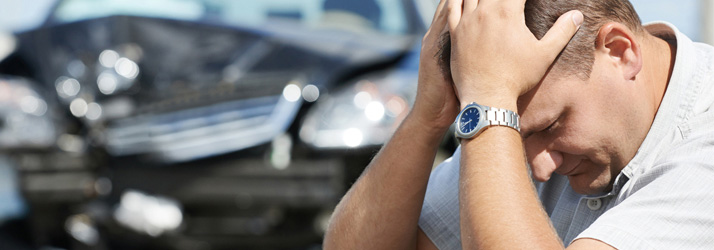 Man holding his neck in pain with damaged car visible in background