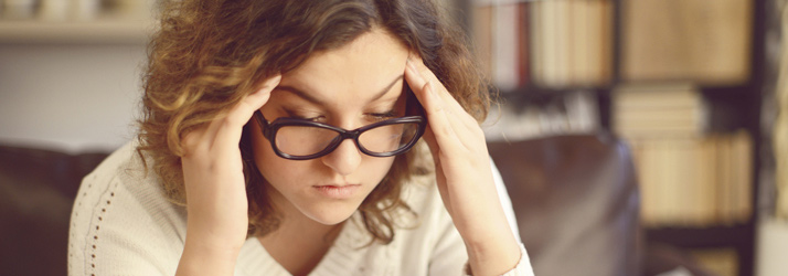 Woman wearing glasses holding her head with both hands, displaying headache discomfort
