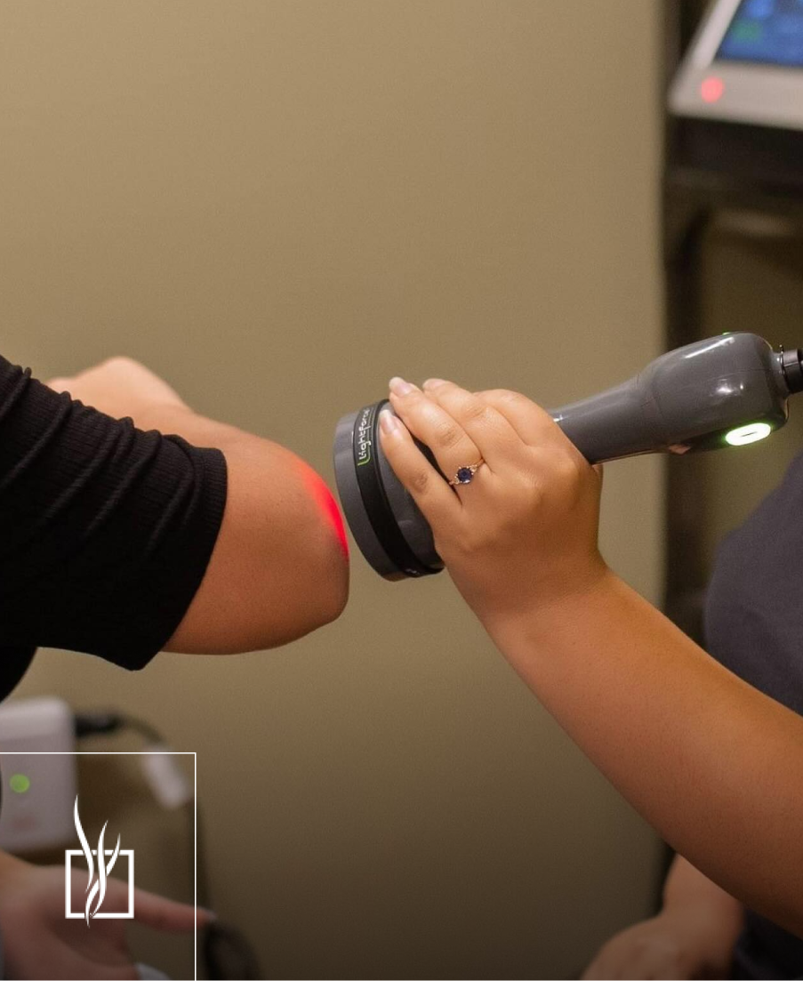 Hands holding handheld infrared therapy device emitting green light on patient's arm during treatment
