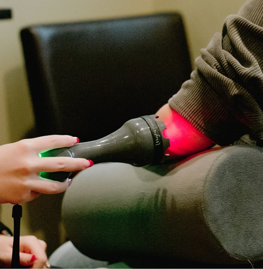 Practitioner applying red light therapy device to patient's shoulder