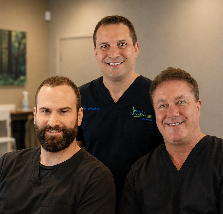 Three chiropractic professionals smiling together in a clinical treatment room