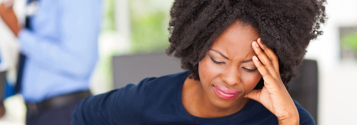 Woman in dark shirt holding her head with hand, displaying migraine or headache discomfort