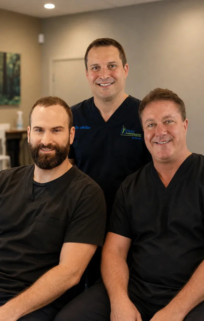 Three chiropractic professionals smiling together in a clinical treatment room