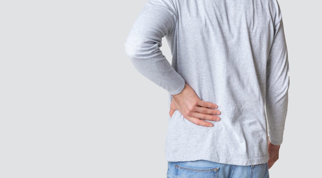 Man in light gray shirt holding lower back with hand