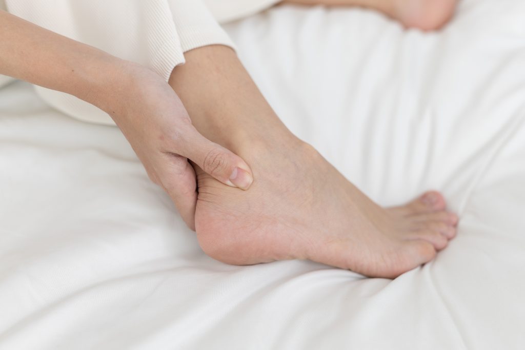 Practitioner's hands palpating patient's ankle on white bedding