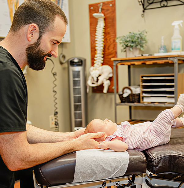 Chiropractor performing spinal adjustment on infant patient lying on treatment table