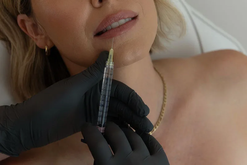 Practitioner in black gloves holding an injection pen near patient's chin for aesthetic treatment
