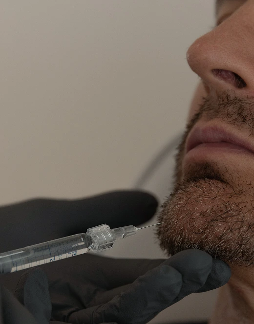 Practitioner holding syringe near man's chin and jawline