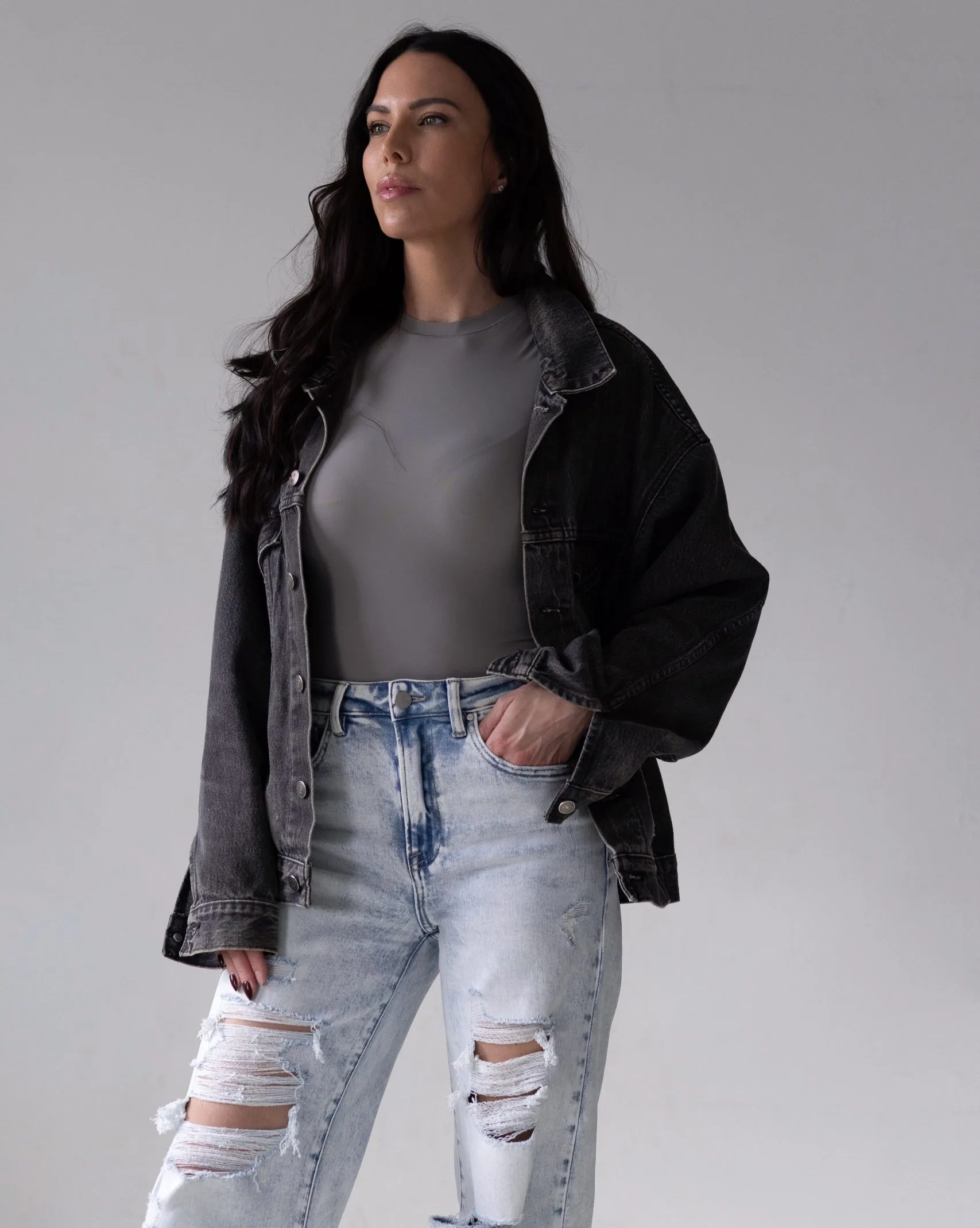 Woman with long black hair wearing a black denim jacket and light blue ripped jeans