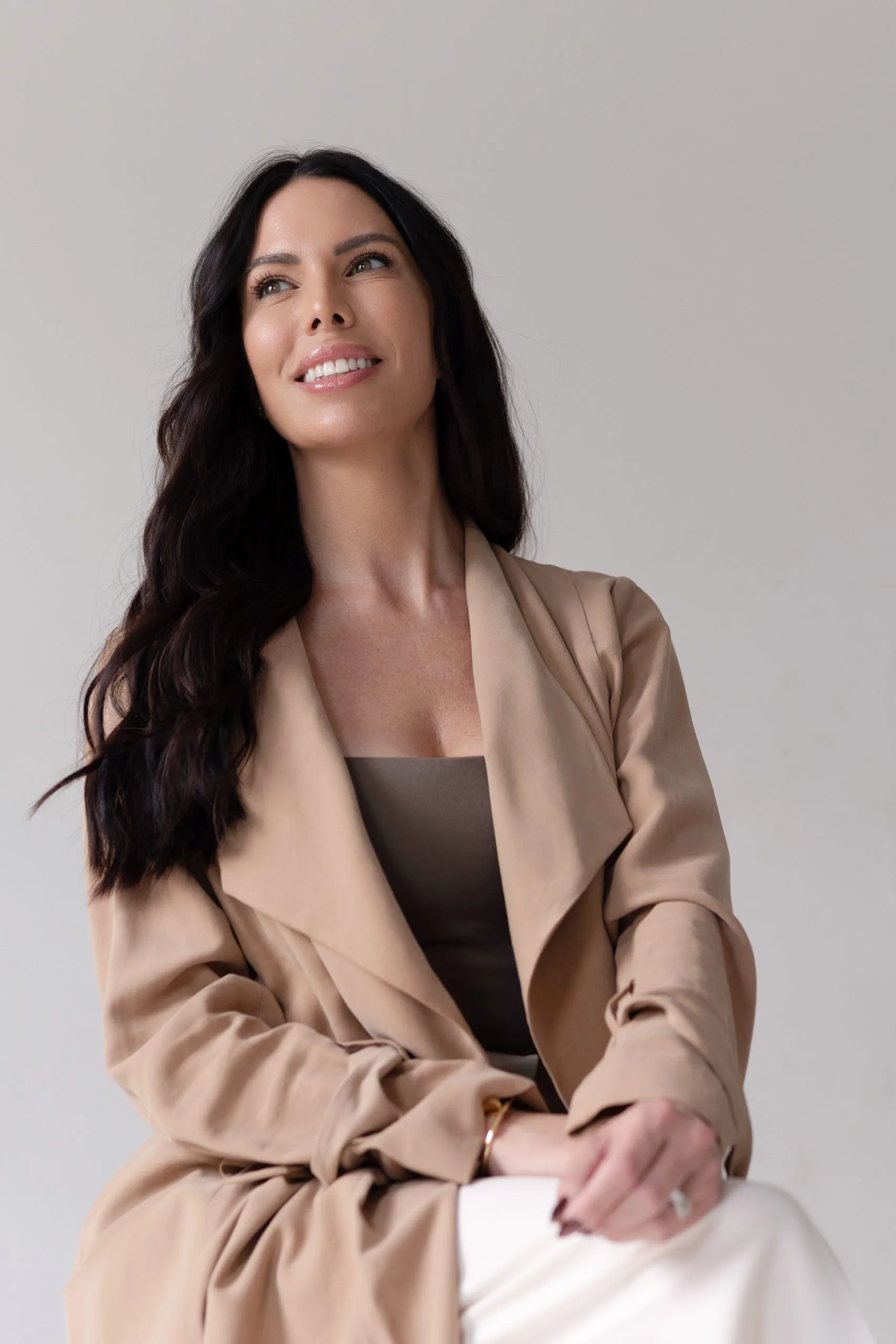 Woman with long dark hair wearing beige blazer, smiling while looking upward