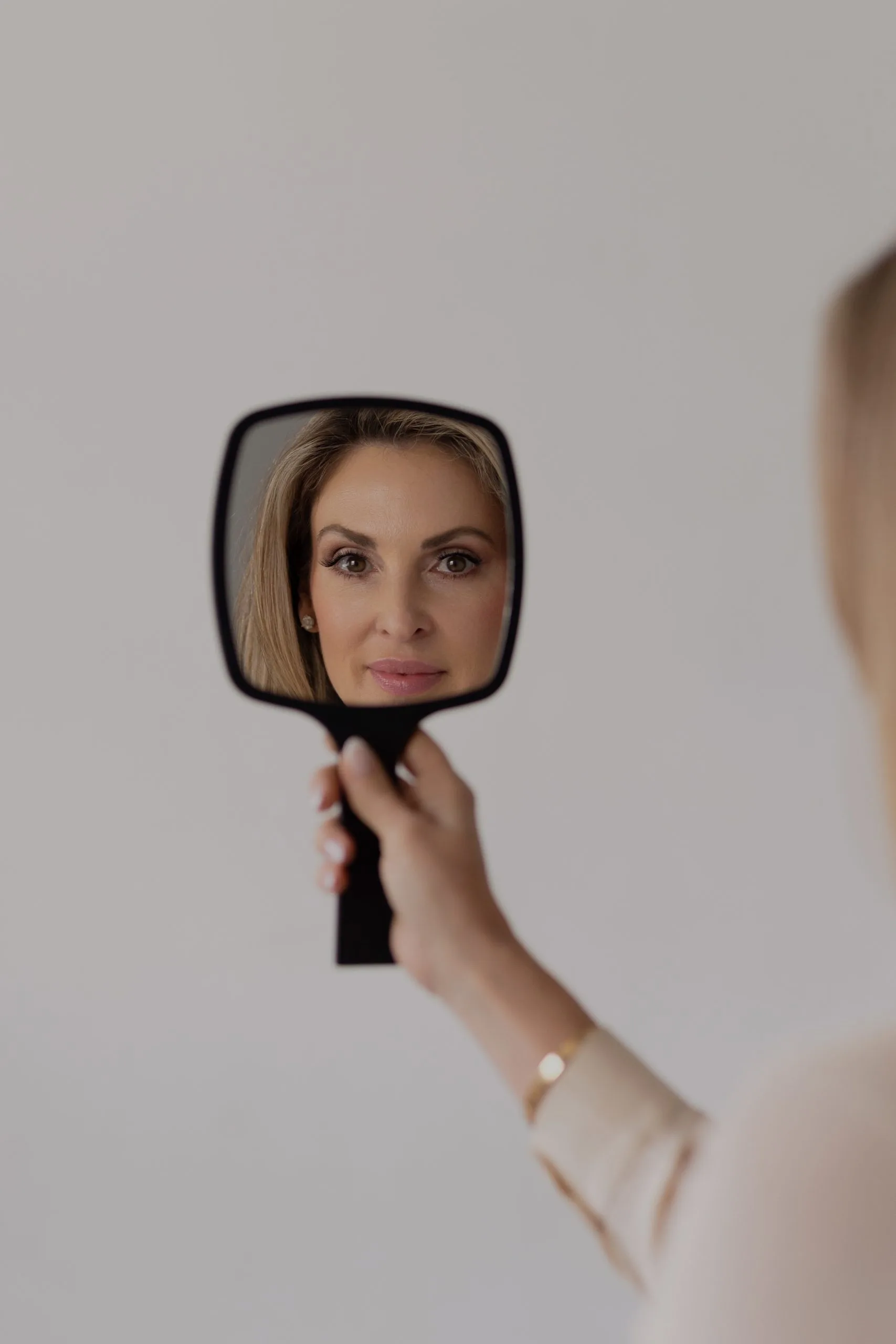 Woman holding hand mirror showing her reflected face