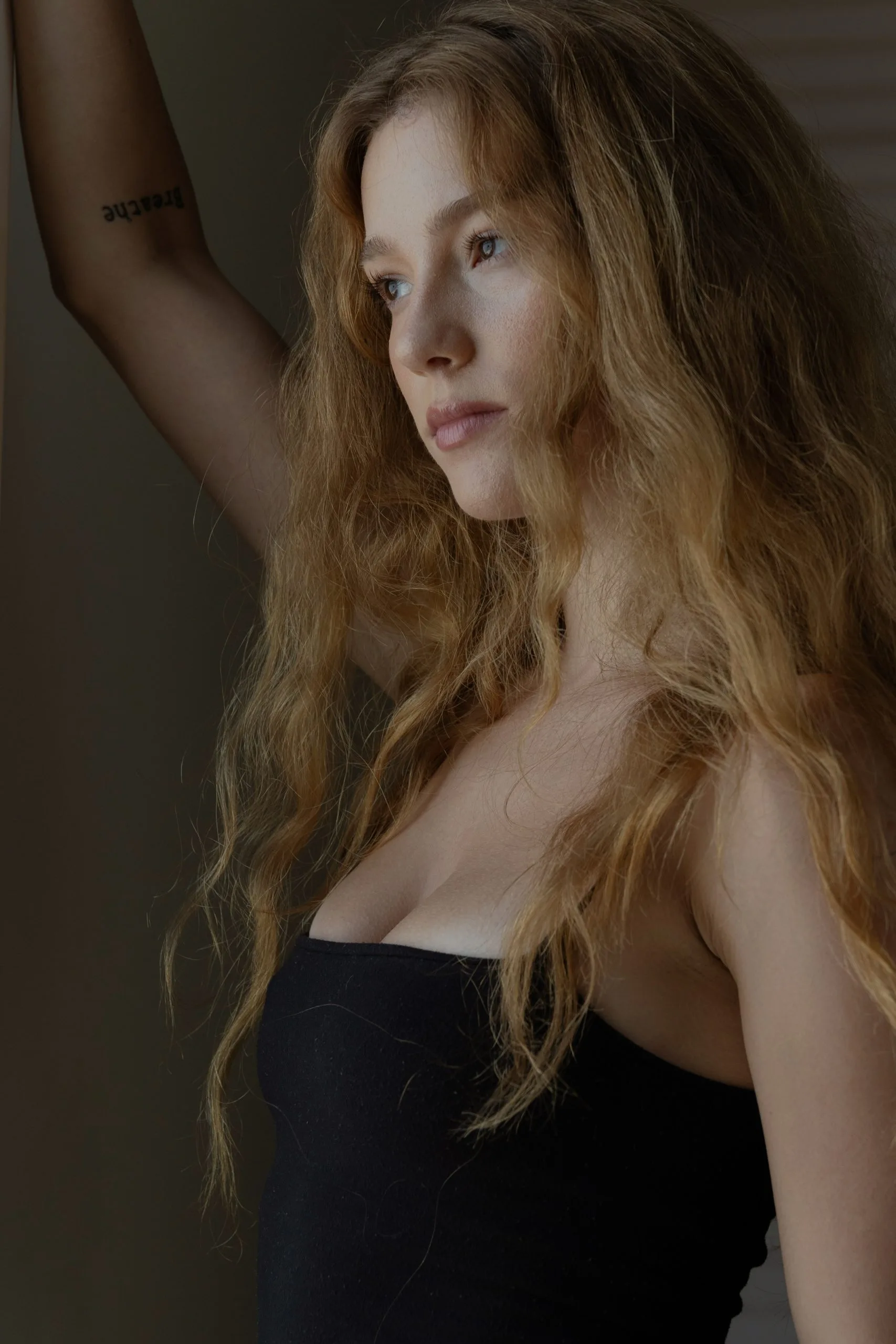 Woman with long wavy blonde hair in profile, wearing black strapless top against neutral background