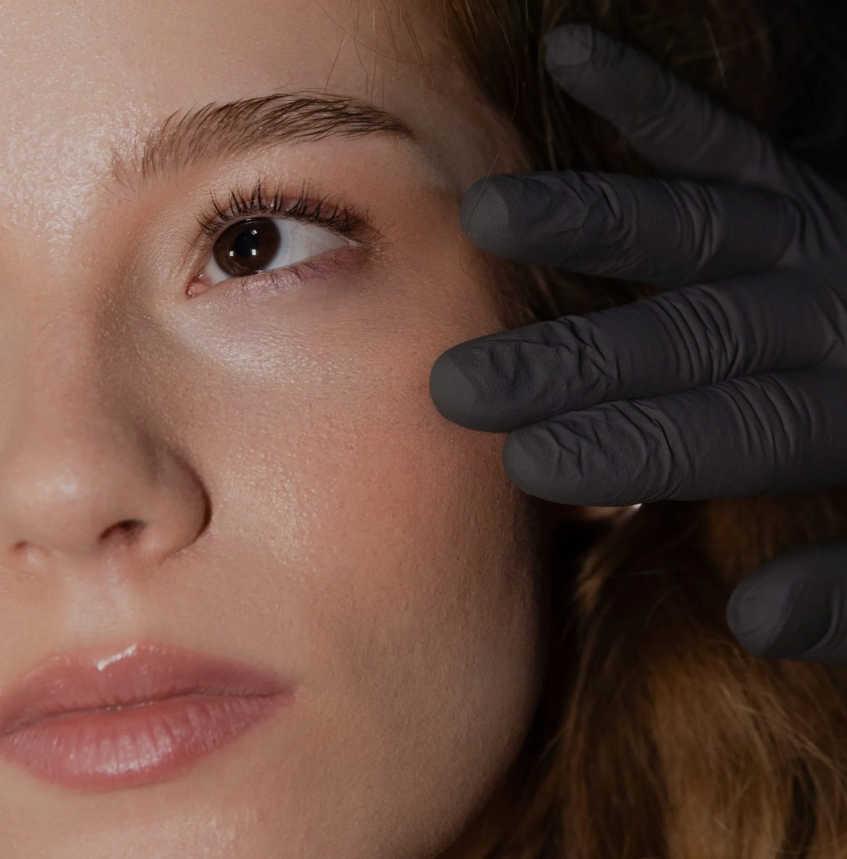 Practitioner in black gloves examining patient's cheek and eye area during aesthetic consultation