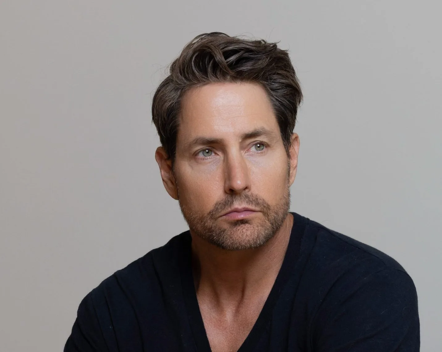 Man with dark hair and facial hair facing forward against neutral background, wearing dark shirt