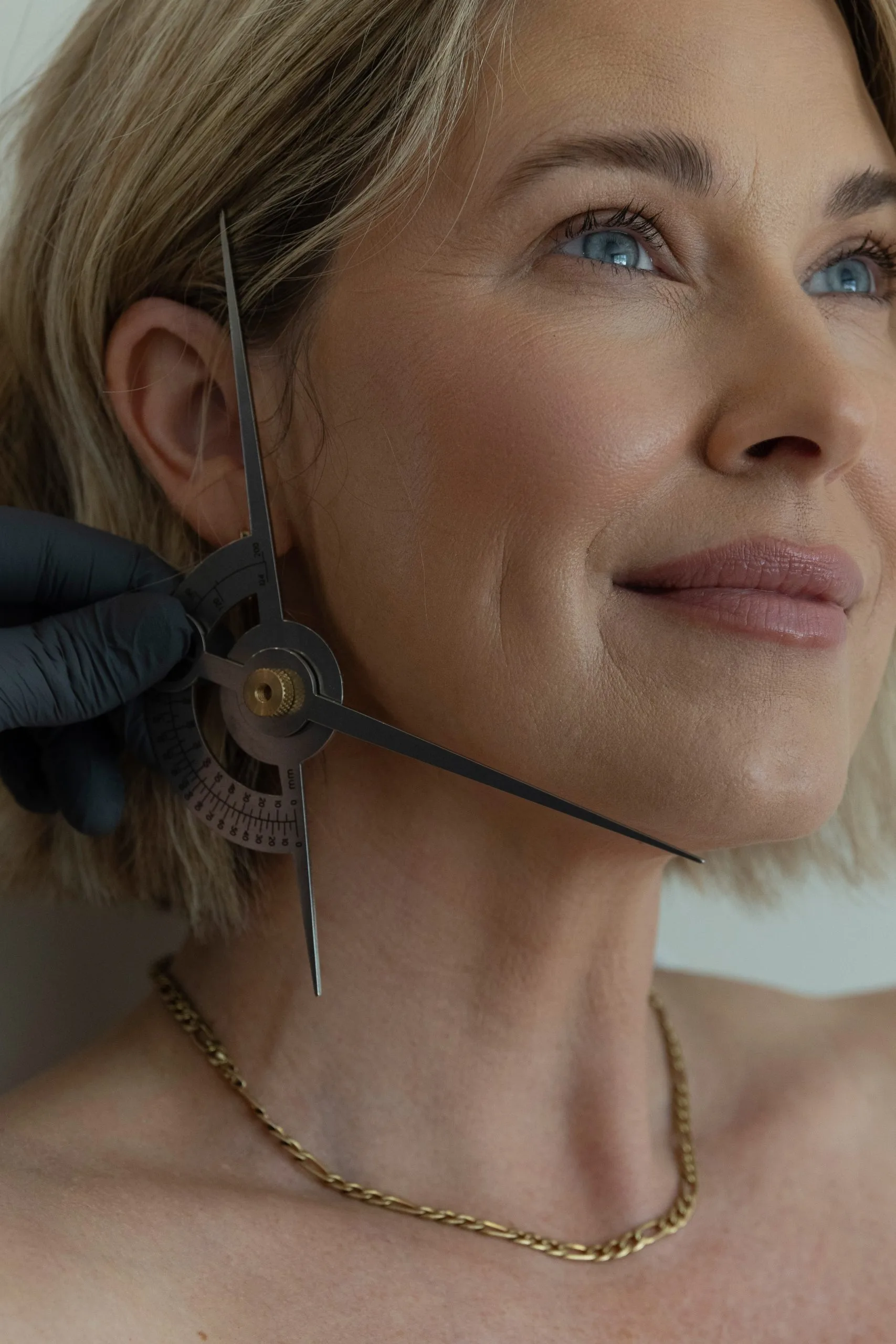 Aesthetician using calipers to measure facial proportions on patient's cheek