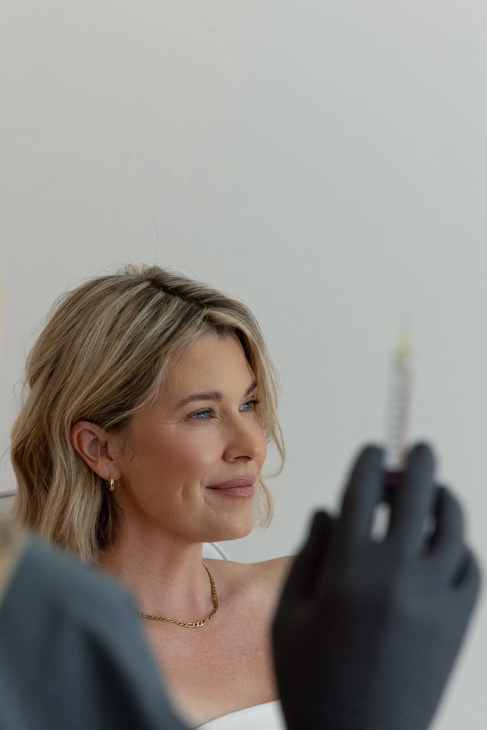 Clinician holding injectable syringe near patient's face during aesthetic treatment