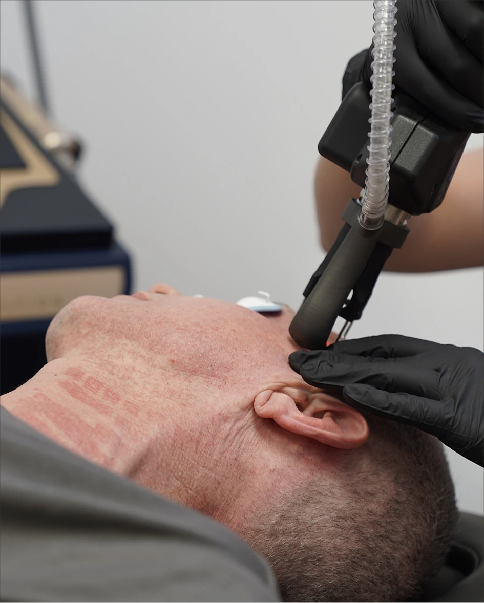 Practitioner using handheld laser device on patient's neck and jawline area