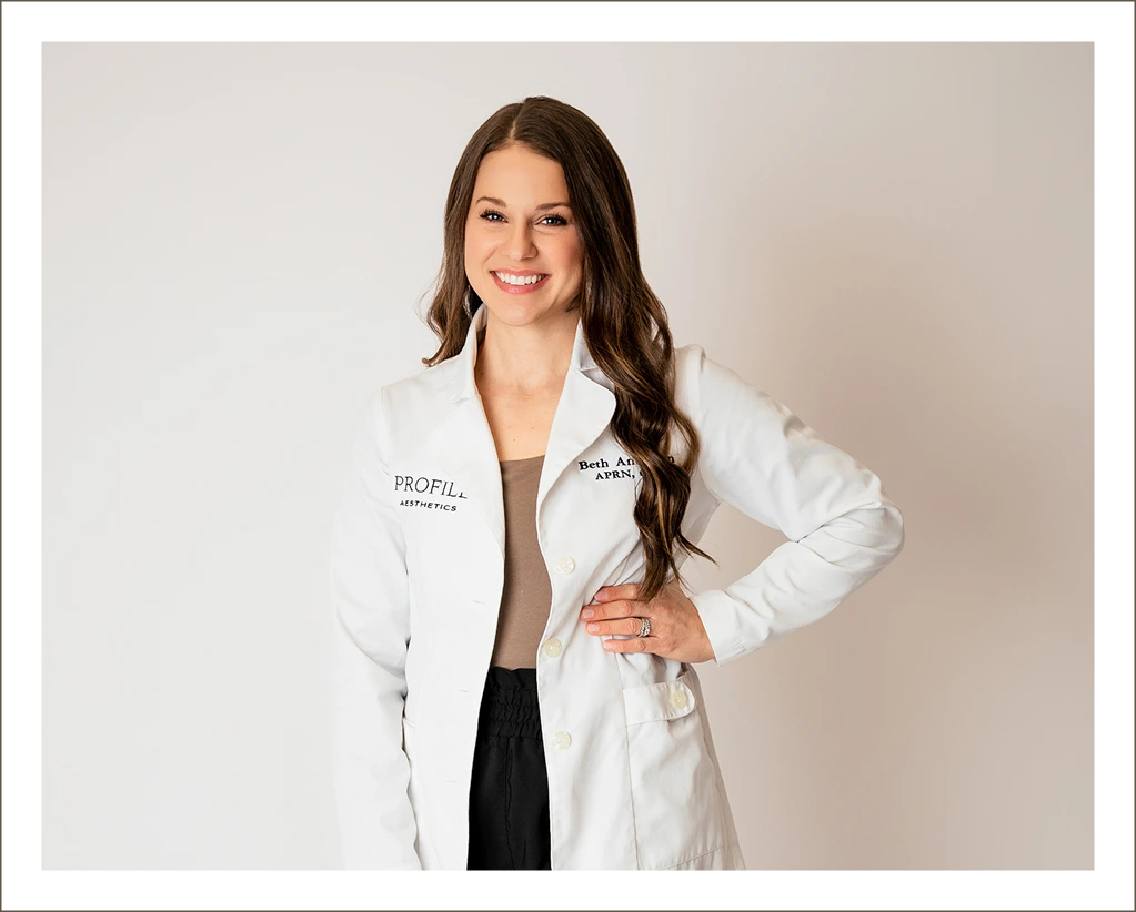 Medical professional in white coat with Profile Aesthetics branding, smiling at camera
