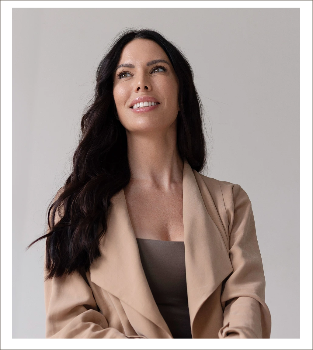 Woman with long dark hair smiling while looking upward, wearing beige blazer
