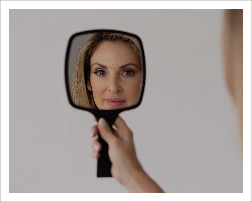 Hand holding black mirror reflecting woman's face for aesthetic assessment