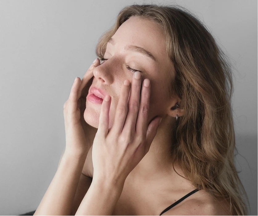 Woman with hands on cheeks displaying healthy, glowing facial skin