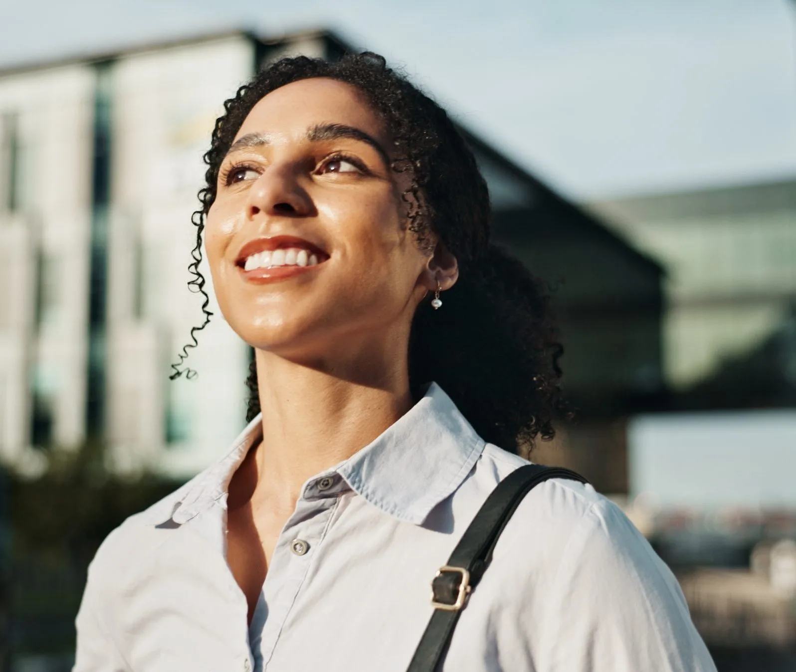 Smiling woman with curly hair outdoors in warm sunlight