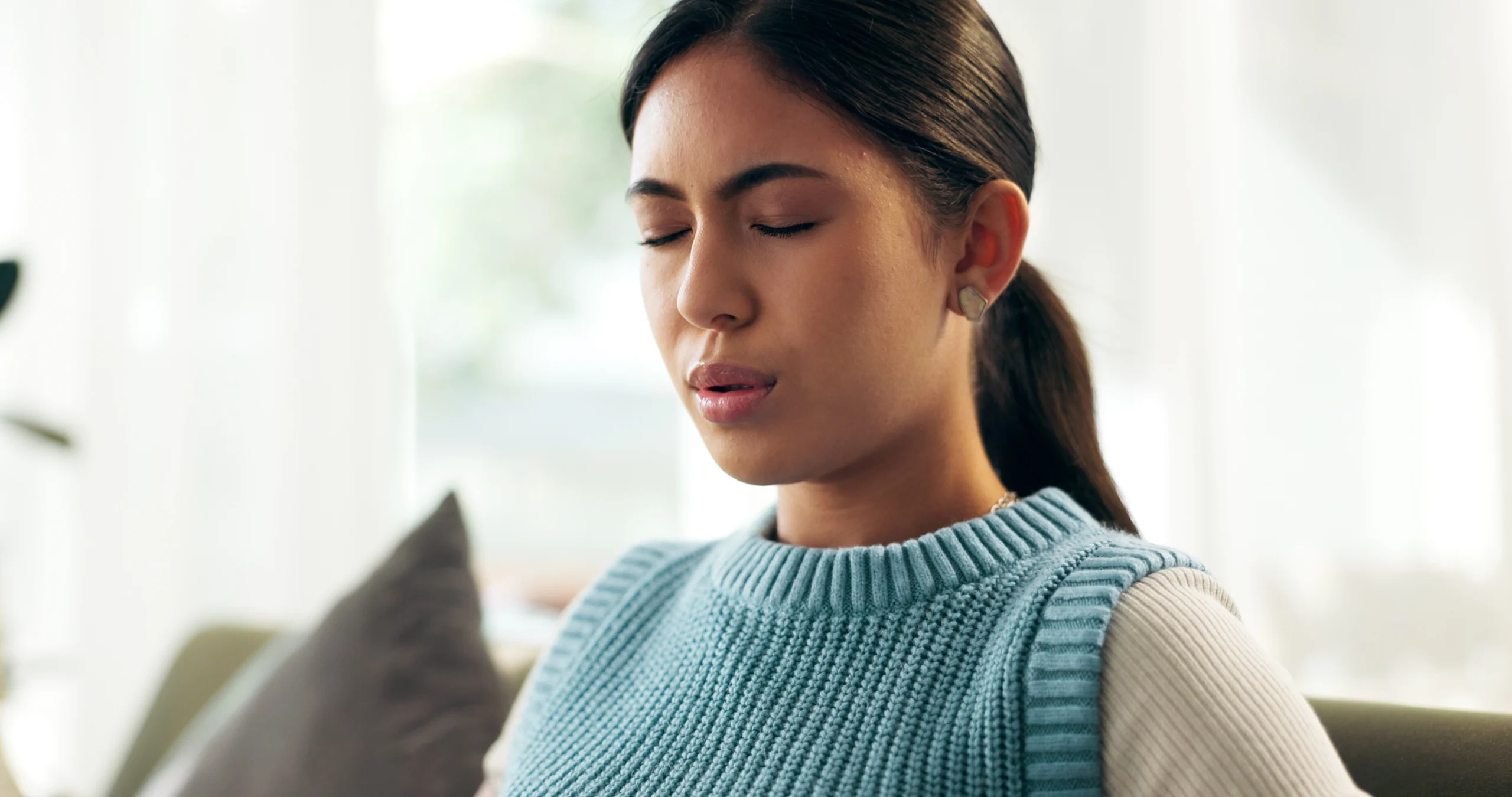 A young woman sits on a sofa with her eyes closed