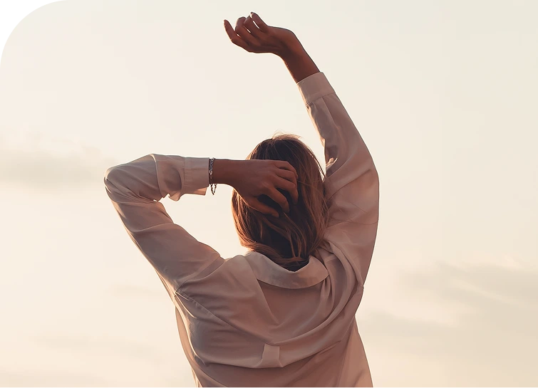 Person from behind with arm raised toward sky in peaceful outdoor setting